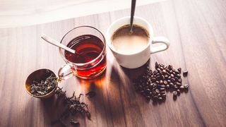 Kaffee oder Tee? Ein Glas Tee und eine Tasse Kaffee stehen auf einem Holztisch