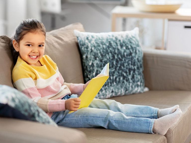 Kleines Mädchen sitzt auf einer Couch und hat ein Buch in der Hand