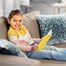 Kleines Mädchen sitzt auf einer Couch und hat ein Buch in der Hand