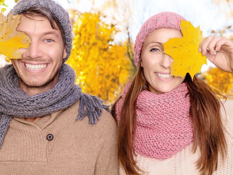 Lachendes Pärchen hält sich je ein Herbstblatt vor ein Auge