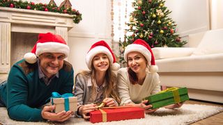 Eltern mit Tochter tragen eine Weihnachtsmütze und haben Geschenke in der Hand