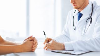 Patientin und Arzt mit Stethoskop sitzen an einem Schreibtisch und man sieht nur dir Hände