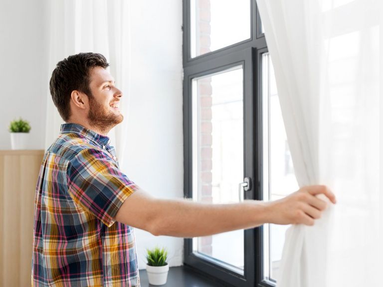 Mann möchte ein Fenster öffnen und schiebt dafür die Gardine beiseite
