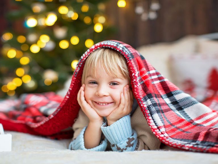 Kleiner, grinsender Junge mit einer karierten Decke auf dem Kopf und im Hintergrund leuchten Lichter