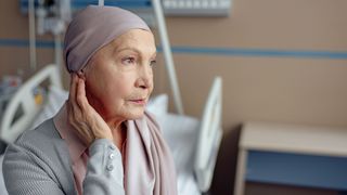 Krebskranke ältere Frau sitzt gedankenverloren in einem Krankenhauszimmer