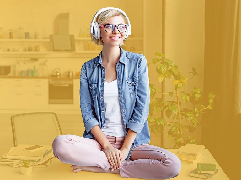 Junge Frau mit Kopfhörern sitzt im Schneidersitz auf eine Tisch