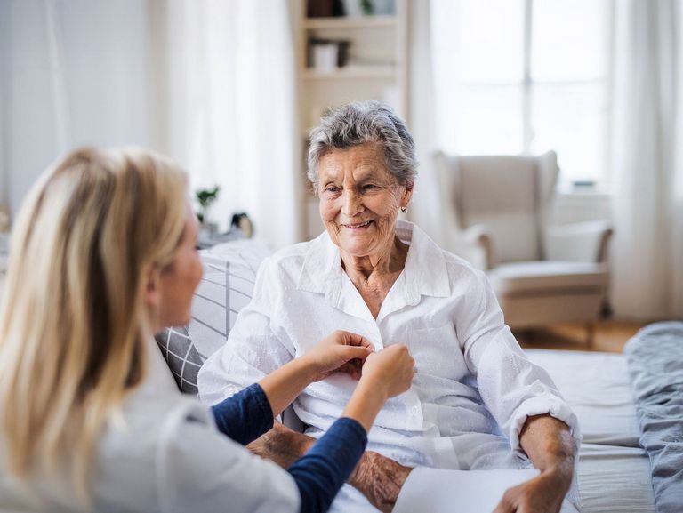 Pflegebedürftige Rentnerin bekommt Hilfe beim Anziehen von einer Pflegekraft
