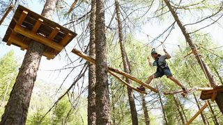 Klettern - Hoch hinaus Mann bewältigt einen Parcours in einem Hochseilgarten