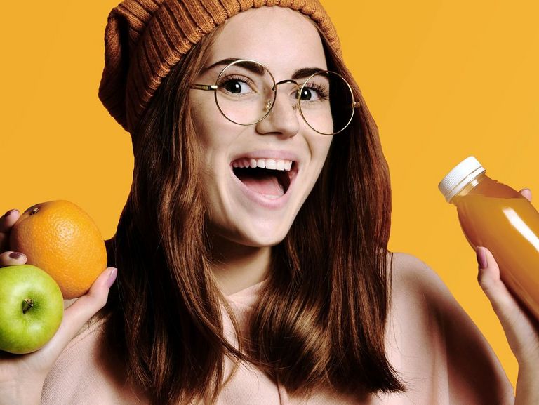 Junge Frau mit einer Orange und einem Apfel in der Hand