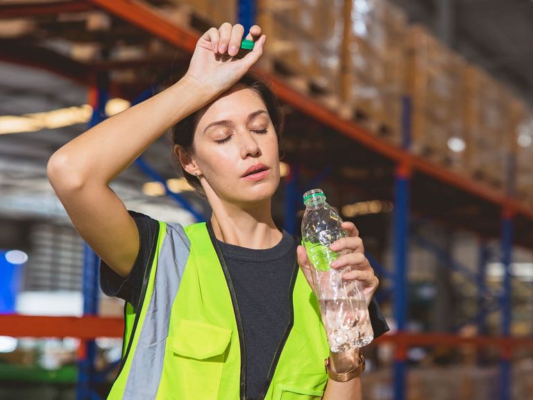 Lageristin ist erschöpft von der Hitze am Arbeitsplatz und hält eine offene Wasserflasche in der Hand
