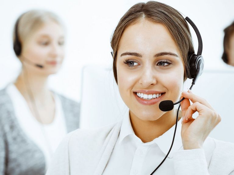 Junge Mitarbeiterin mit einem Headset führt gerade ein Telefongespräch