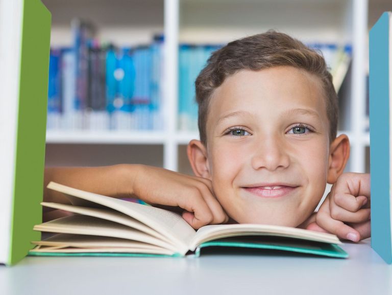 Junge schaut durch ein Bücherregal hindurch