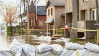 Das "Handwerk hilft" in den Hochwasserregionen Hochwasser vor einer Häuserfront mit einer Barriere aus Sandsäcken im Bildvordergrund