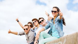 Gruppe Jugendlicher mit Sonnenbrillen sitzen auf einer Mauer und jubeln mit Daumen hoch