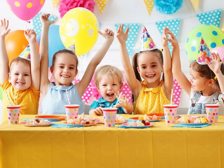 Fünf kleine Kinder jubeln mit erhobenen Armen inmitten bunter Geburtstagsdekoration