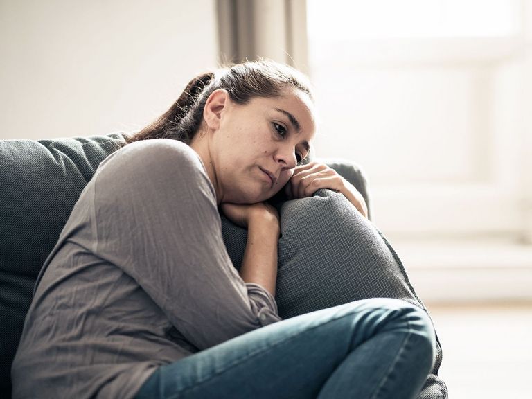 Frau liegt traurig und melancholisch gestimmt auf einer Couch