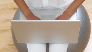 Frau benutzt Laptop sitzend auf Gesundheitsball