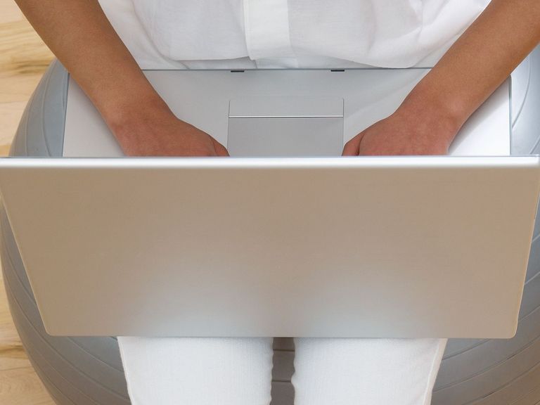 Frau benutzt Laptop sitzend auf Gesundheitsball
