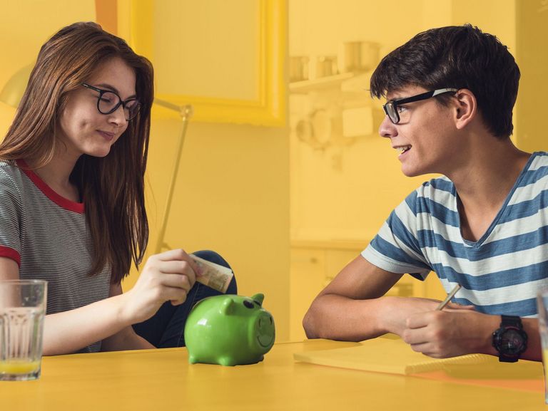 Zwei Teenager befüllen ein grünes Sparschwein