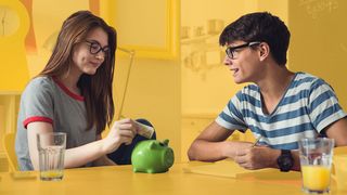 Zwei Teenager befüllen ein grünes Sparschwein