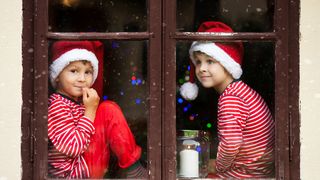 Zwei Jungen mit Weihnachtsmützen schauen durch ein geschlossenes Fenster heraus