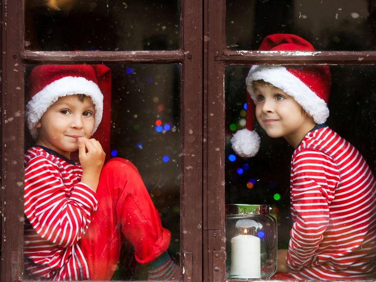 Zwei Jungen mit Weihnachtsmützen schauen durch ein geschlossenes Fenster heraus