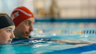 Sicheres Schwimmtraining Vater und Tochter mit Badekappen in der Schwimmhalle beim Schwimmtraining