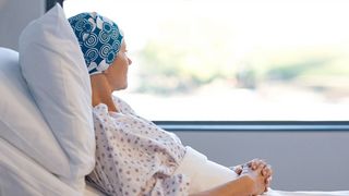 Krebskranke Frau schaut gedankenverloren von ihrem Krankenhausbett aus dem Fenster
