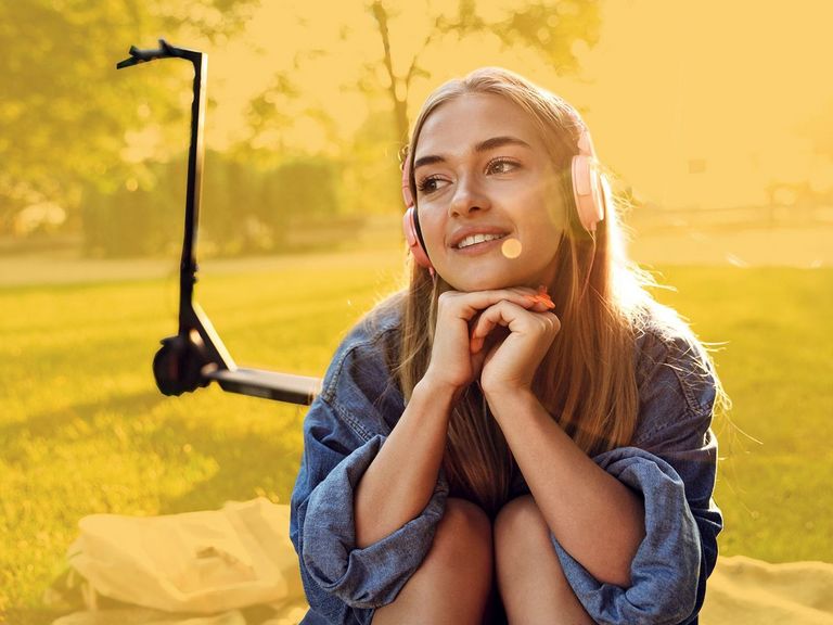Jugendliche mit Kopfhörern und eRoller sitzt auf einer Decke im Park