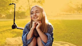 eScooter & eRoller Jugendliche mit Kopfhörern und eRoller sitzt auf einer Decke im Park