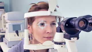 Frau schaut durch ein Messinstrument beim Augenarzt