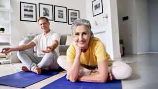 Paar sitzt für eine Meditation im Wohnzimmer auf einer Matte