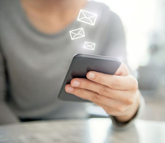 Frau hält ein Smartphone in der Hand und darüber schweben kleine stylisierte Briefumschlag-Icons
