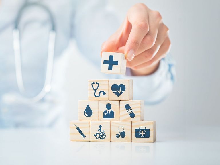 Würfelpyramide mit Symbolen aus dem Gesundheitswesen und einer Ärztin mit Stethoskop im Hintergrund