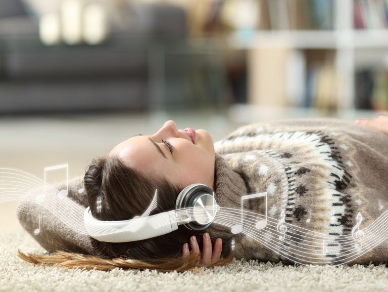 Frau mit Kopfhörern liegt auf einem Teppich und hört zufrieden ihre Lieblingsmusik