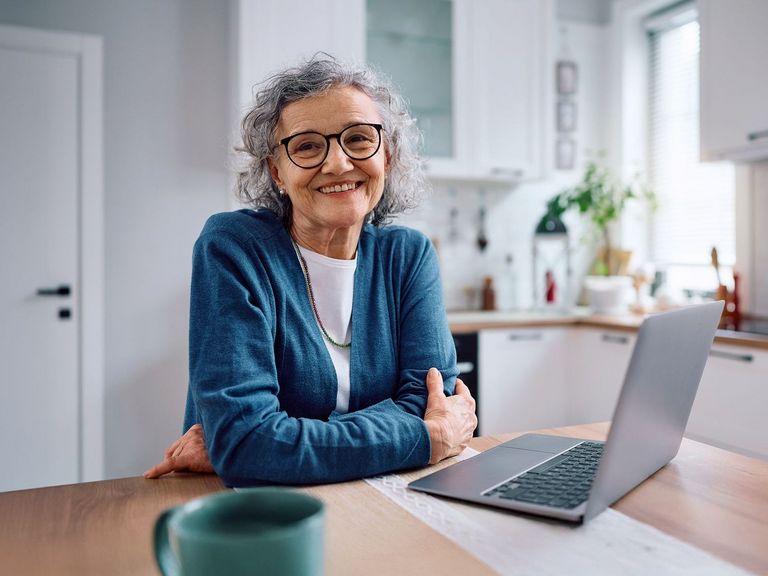 Älter Frau sitzt in der Küche vor einem Laptop