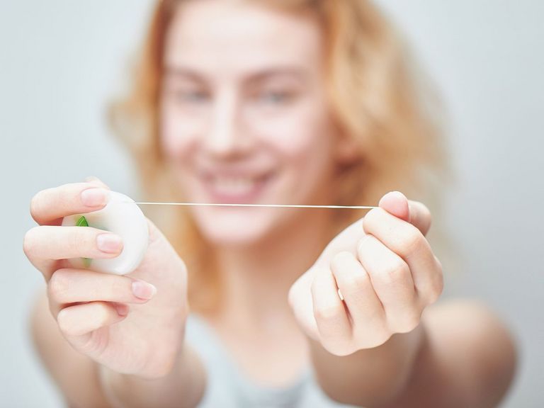 Junge Frau hält Zahnseide in die Kamera