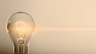 Energiesparen Glimmende Glühlampe vor blau-grauem Hintergrund