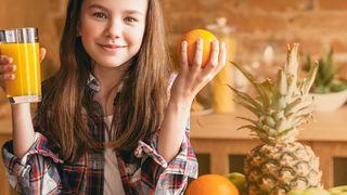Jugendliches Mädchen hält ein Glas mit Orangsaft und eine Orange jeweils in einer Hand