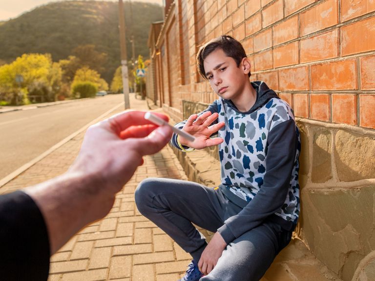 Jugendlicher, an einer Wand hockend, lehnt mit verneinender Geste eine Zigarette ab