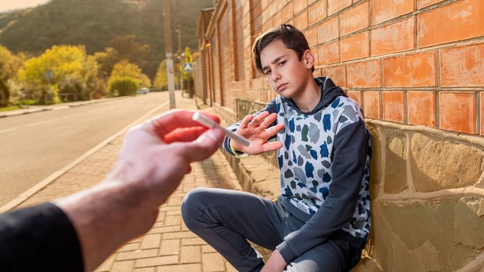 Jugendlicher, an einer Wand hockend, lehnt mit verneinender Geste eine Zigarette ab