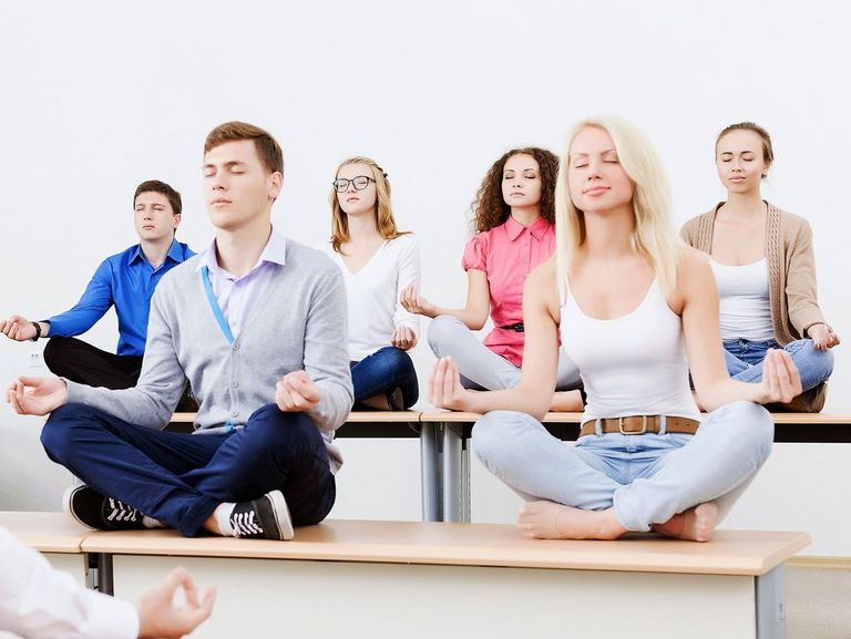 Schüler sitzen auf Schülertischen im Schneidsitz