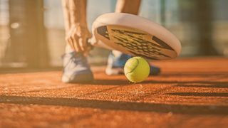 Nahaufnahme eines Padel-Tennis-Schlägers dicht über dem Boden mit einem Tennisball