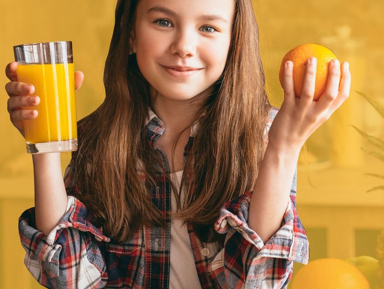 Mädchen hält ein Glas mit Orangensaft und eine Orange