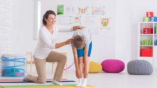 Sporttherapeutin trainiert mit einem Jungen die Rückenmuskulatur