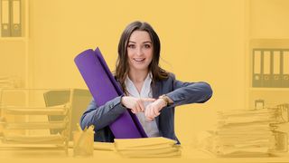 Azubi sitz an einem vollem Schreibtisch mit Yogamatte und zeigt auf die Uhr	