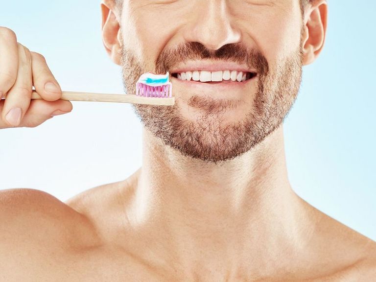 Mann mit Bart und gepflegten Zähnen hält eine Zahnbürste in der Hand