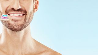 Mann mit Bart und gepflegten Zähnen hält eine Zahnbürste in der Hand