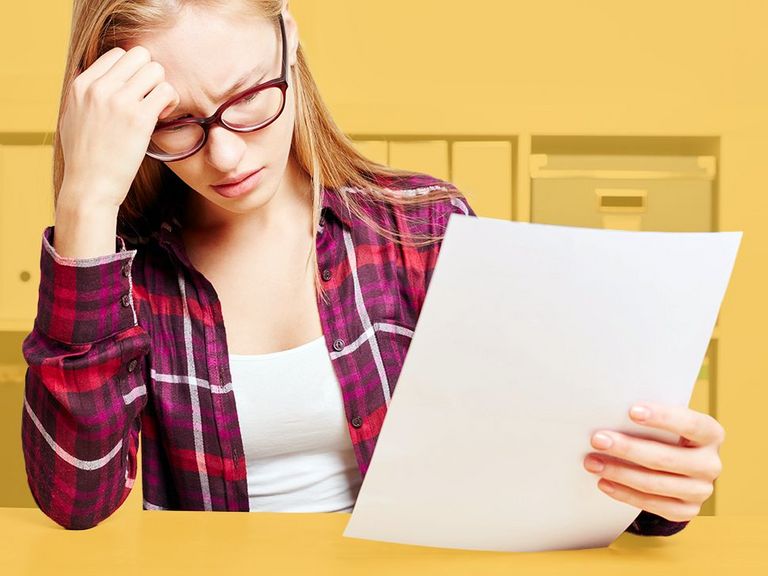 Junge Frau am Schreibtisch sitzend liest etwas auf einem Blatt Papier