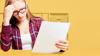 Junge Frau am Schreibtisch sitzend liest etwas auf einem Blatt Papier